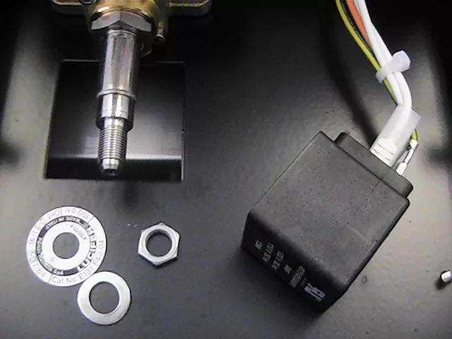 Close-up of electrical components, including a metal shaft, black relay switch, nut, washers, and multicolored wires secured with a zip tie—commonly seen during OPV adjustment on a Rancilio Silvia espresso machine. © 2025 1st-line.com