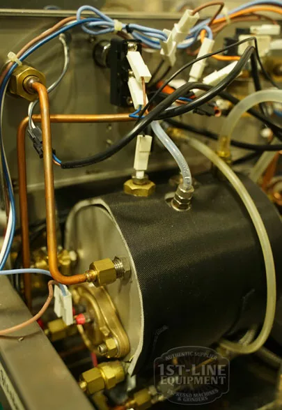 Close-up of the Elektra Verve Dual Boiler Espresso Machine’s internal parts, featuring metal pipes, wires, and connectors on the cylindrical dual boiler. The image has a 1st-Line Equipment watermark. © 2025 1st-line.com
