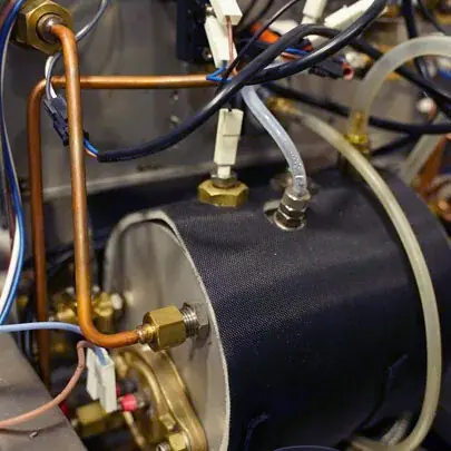 Close-up of mechanical and electrical components, including copper pipes, wires, connectors, and a cylindrical metal part&mdash;possibly part of Elektra Verve equipment used to prevent boiler overheating or manage coffee steam.