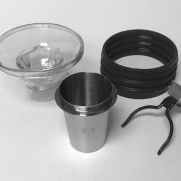 A set of coffee brewing accessories—glass funnel, stainless steel cup, black silicone ring, and metal filter holder—perfect for use with the Eureka Mignon Single Dose Kit, all neatly arranged on a white surface. © 2025 1st-line.com