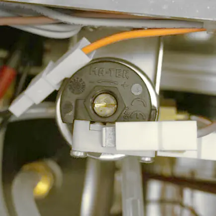Close-up view of an electrical component labeled HA-TER on its circular, black plastic surface&mdash;part of the Elektra Verve steam boiler system. Orange and white wires are attached, with metal and plastic parts visible around it for precise pressure adjustment. &copy; 2025 1st-line.com