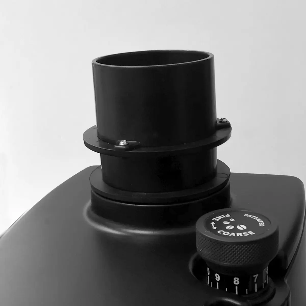 Close-up of a black machine part on an Eureka Atom W 65 Weight Based Espresso Coffee Grinder, showcasing a cylindrical tube and labeled coarse adjustment dial against a plain light background. © 2025 1st-line.com