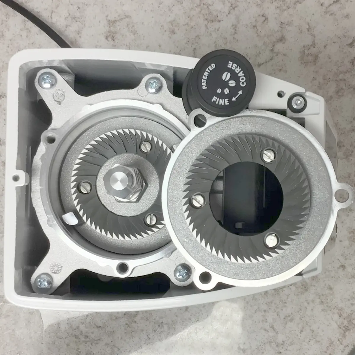 Close-up of the Eureka Atom W 65 Weight Based Espresso Coffee Grinder, showing its inner metal burrs with sharp teeth, screws, and a dial labeled Rotated, Coarse, and Fine on a speckled countertop. © 2025 1st-line.com